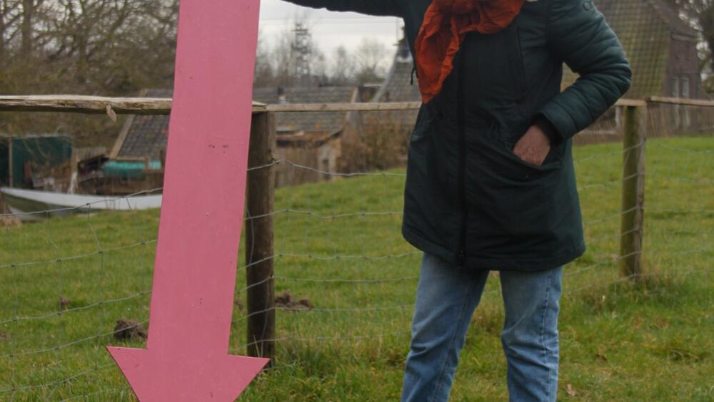 Een vrijwilliger met naast zich een mensgrote roze pijl die wijst naar het gras