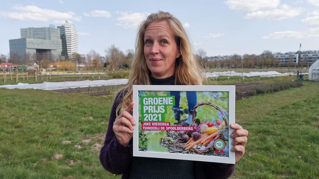 Joke Wierenga met in haar handen de Groene Prijs: een ingelijste oorkonde. Op de achtergrond de moestuin.