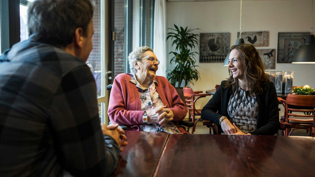 Een jonge en een oude vrouw zitten samen aan tafel en lachen naar elkaar
