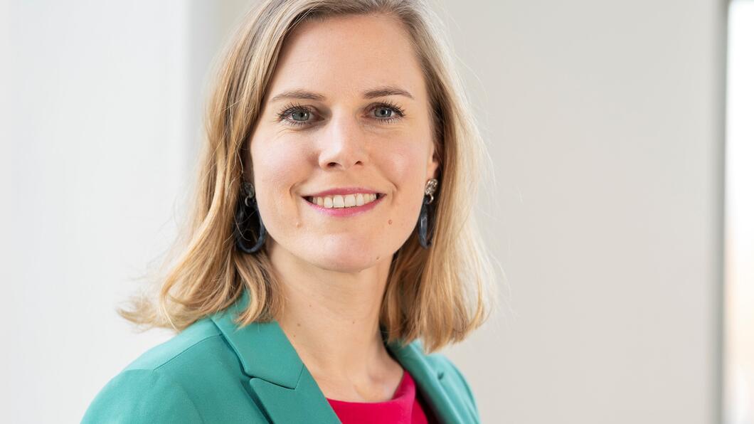 Dorrit de Jong met blond haar, een groen jasje en een rood shirt aan. Ze lacht naar de camera.