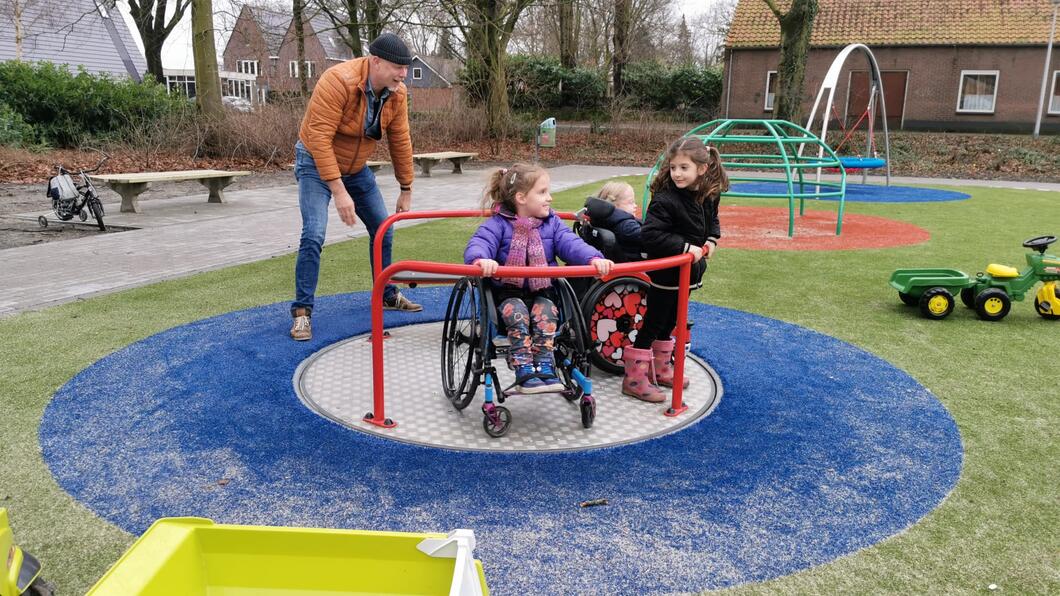 Een man duwt een draaimolen met daarin drie kinderen, van wie twee in een rolstoel zitten