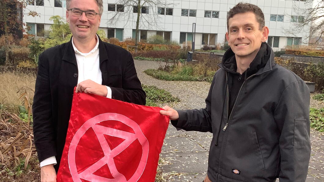 Martin en Rob houden een rode vlag met het symbool van XR erop vast.