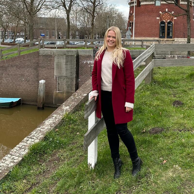 Esmee Pater staat aan een waterkant. Ze heeft blond haar, en een rode jas aan
