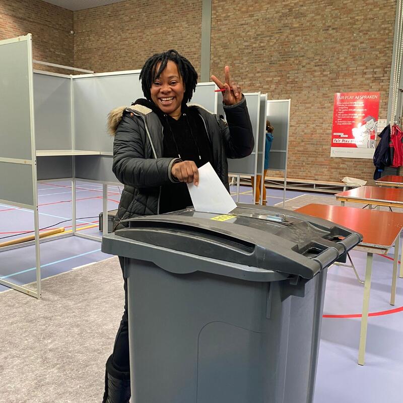 Miriam Ntumba stemt voor de gemeenteraadsverkiezingen. Ze gooit haar stembiljet in een grijze stembus.