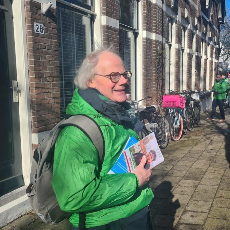 Jan Woltinge met een groen GroenLinks-jasje aan op straat met flyers in zijn hand