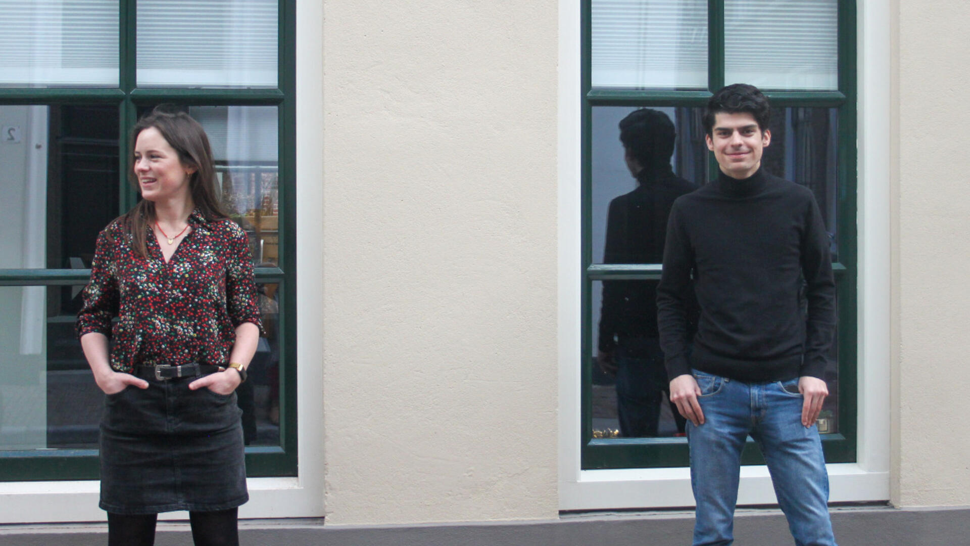 Simone en Romano Boshove, elk staande voor een raam. Simone staat links en kijkt naar links, Romano staat rechts en kijkt naar voren.