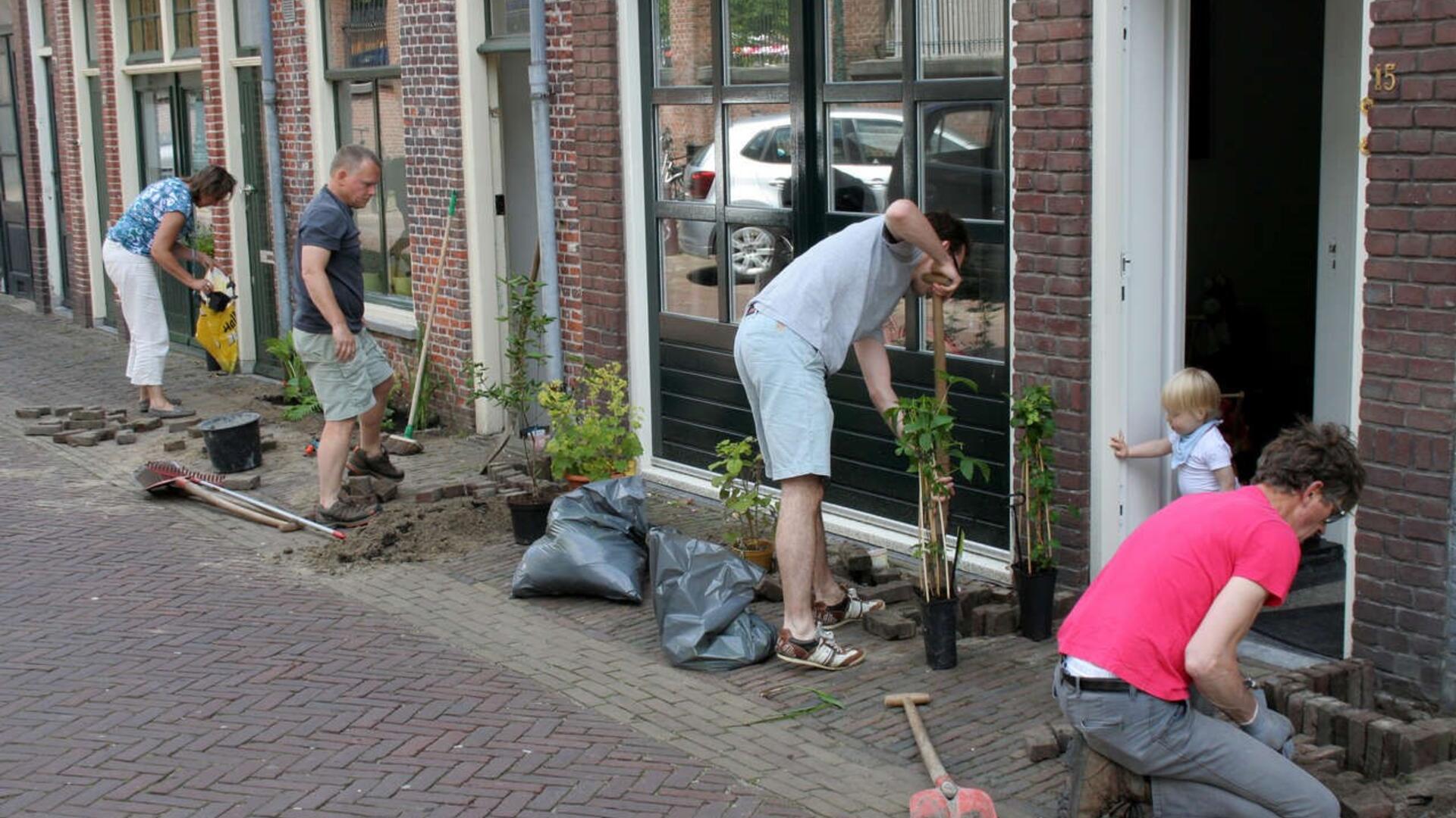 Verschillende mensen die bij huizen in een straat geveltuintjes aan het aanleggen zijn.