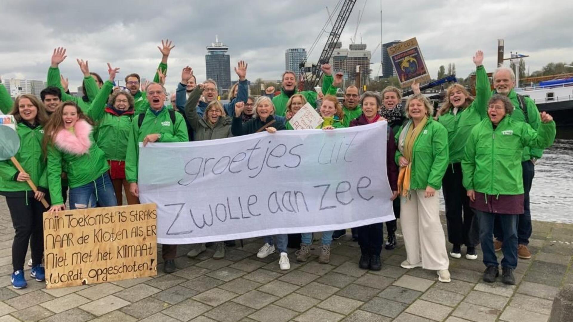 Tientallen Zwollenaren bij de klimaatmars. Ze hebben groenlinks-jasjes aan en houden een spandoek vast waarop staat: 'groetjes uit Zwolle aan zee'