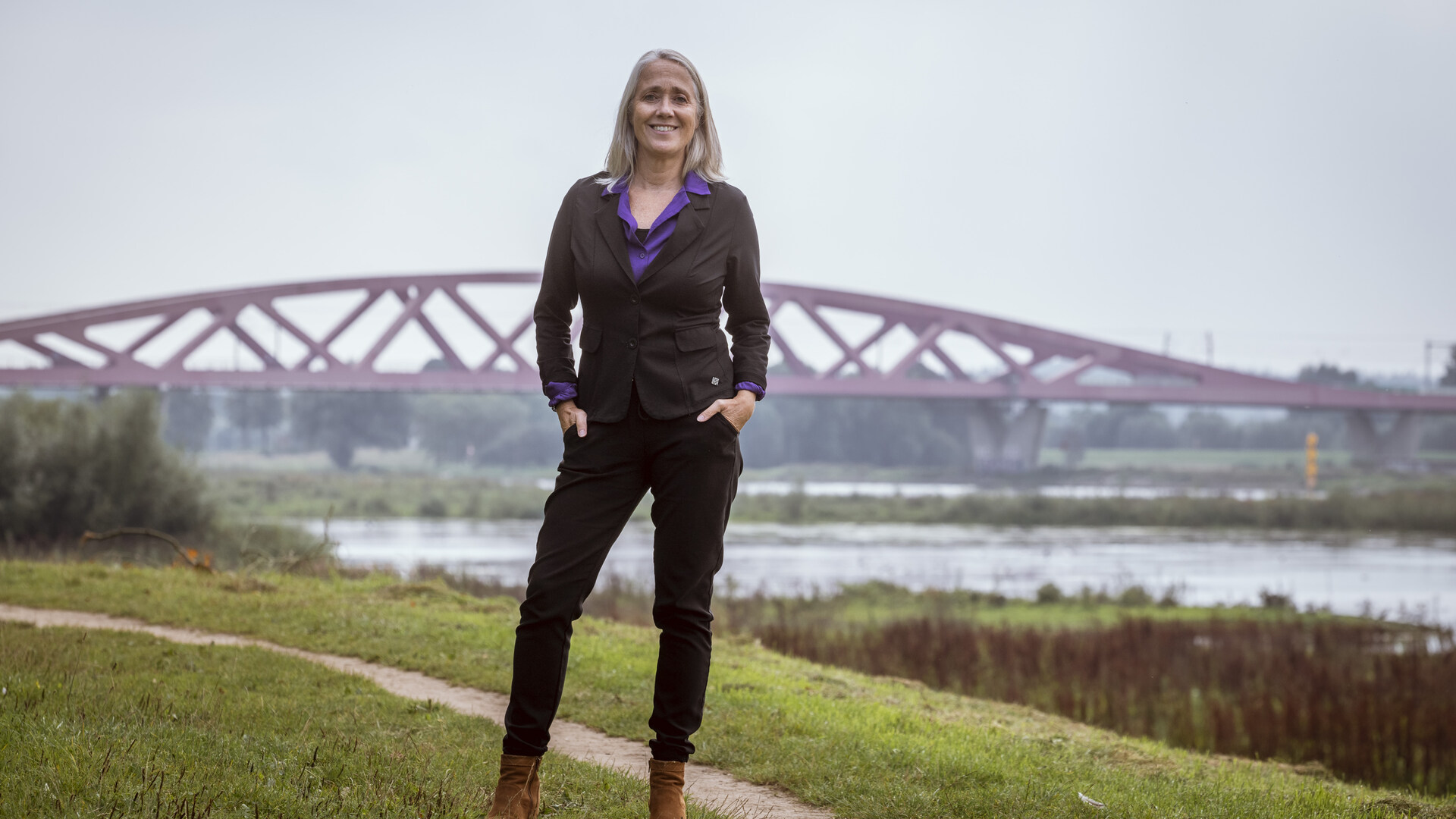 Anja Roelfs staat op de IJsseldijk. Achter haar is de IJsselbrug te zien.