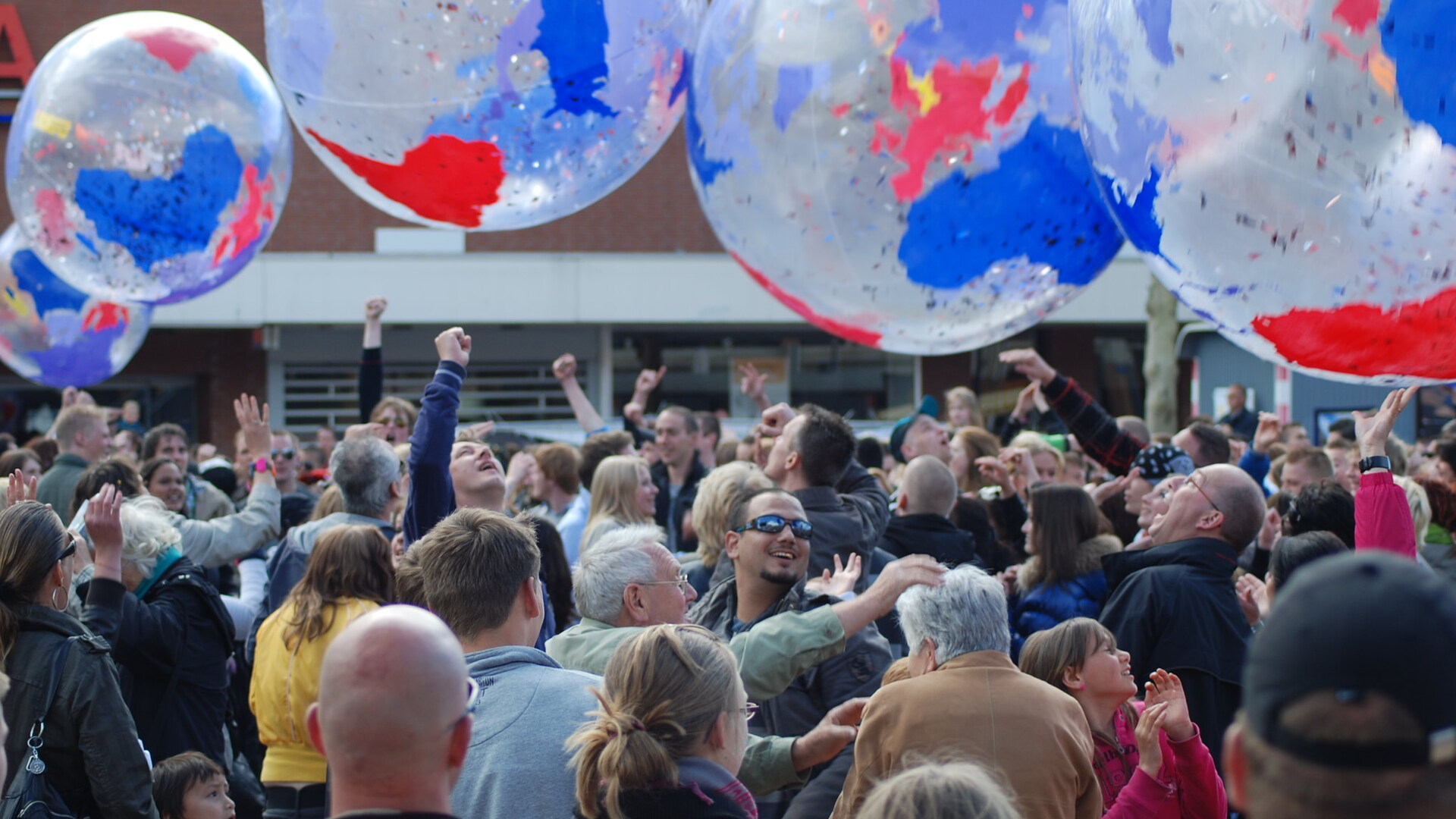 Een plein vol mensen, met boven hun hoofden grote plastic ballen met daarop de aarde afgebeeld.