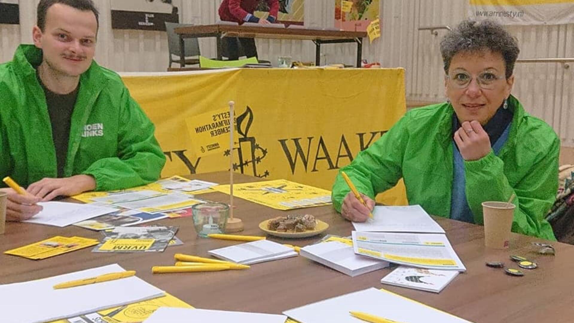 Stan Vergeer en Margriet Leest aan de Amnesty-schrijftafel. Ze hebben allebei een groen jasje aan.