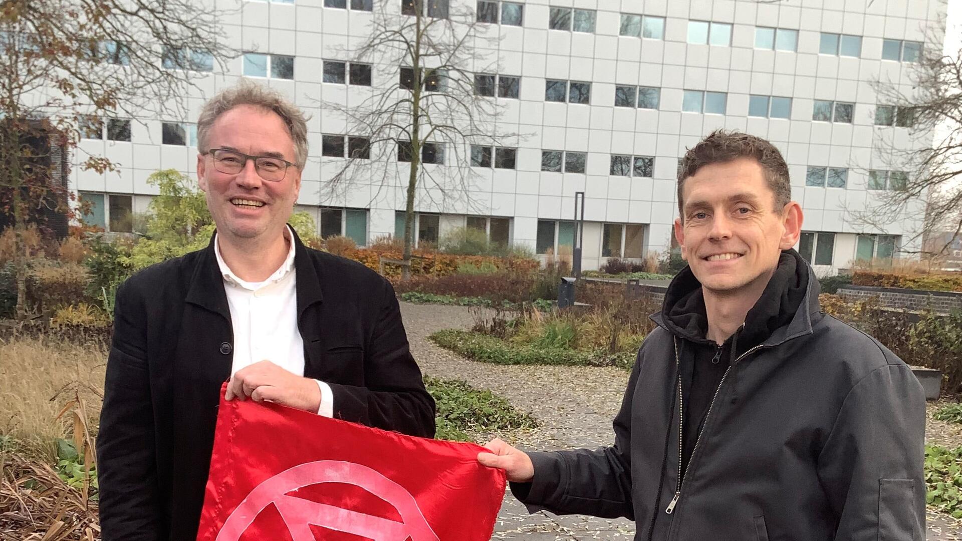 Martin en Rob houden een rode vlag met het symbool van XR erop vast.