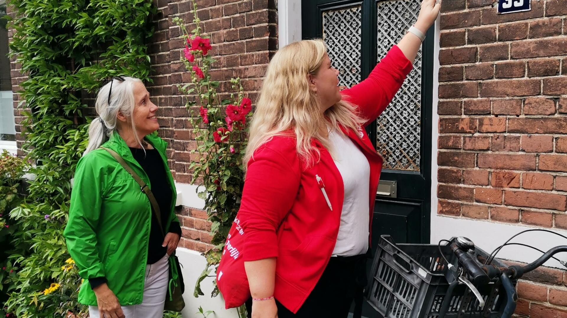 Een vrijwilliger met een rood pvda-jasje aan belt aan bij een voordeur. Een vrijwilliger met een GroenLinks-jasje aan staat ernaast.