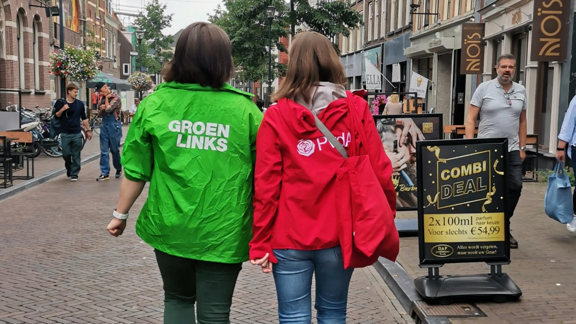 Twee vrijwilligers lopen door een straat, een met een GroenLinks- jasje, een met een PvdA-jasje