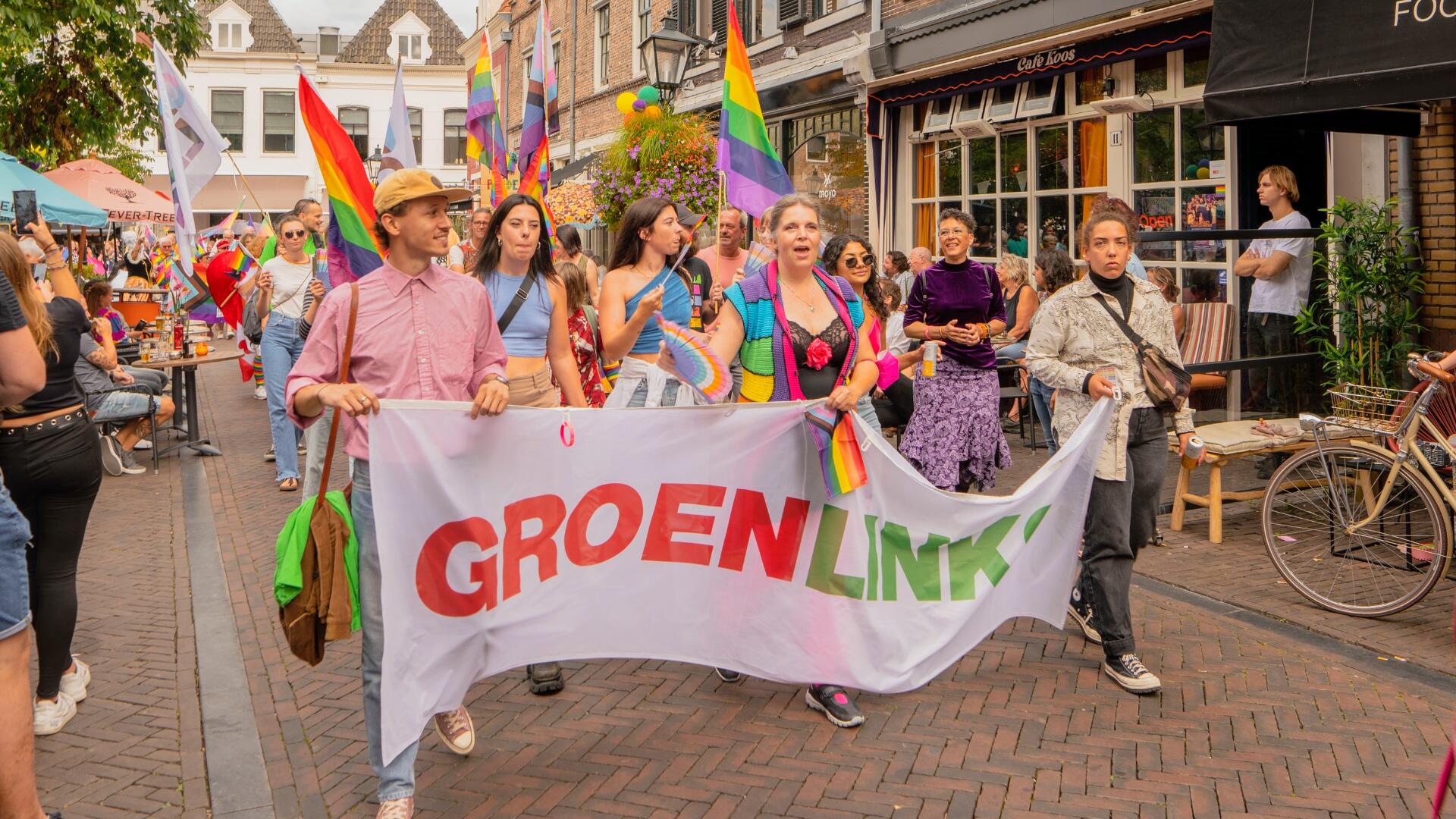 Een groep mensen in de Pride Walk. Ze houden een vlag met 'GroenLinks' erop vast.